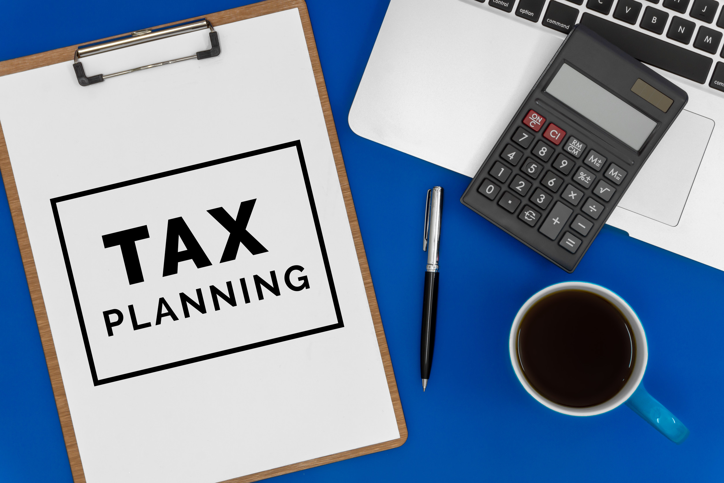 Tax Planning on Paper Top View of Laptop, Calculator and Coffee Cup on Blue Office Desk Business concept